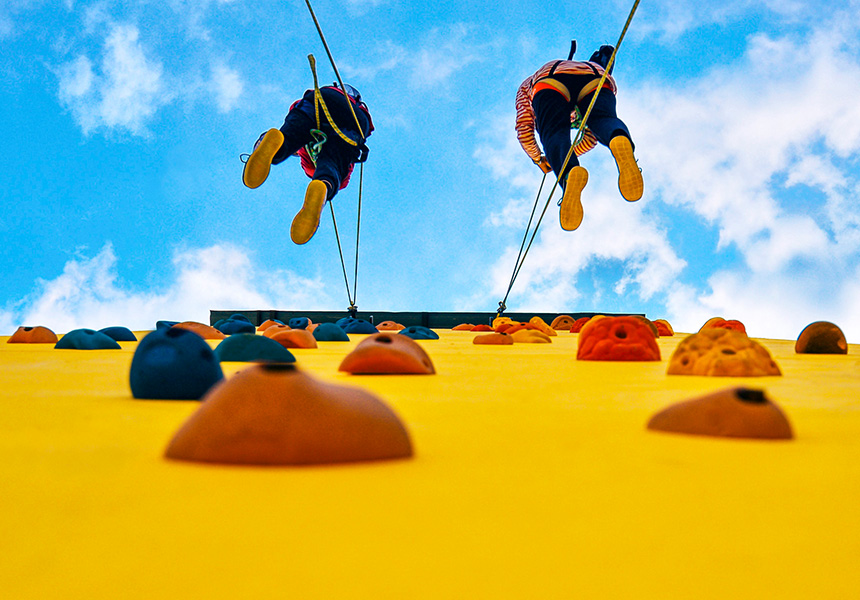 A view from below two climbers scaling a rock climbing wall.